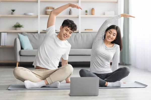Весела азіатська сім'я практикує йогу вдома, використовуючи ноутбук — стокове фото