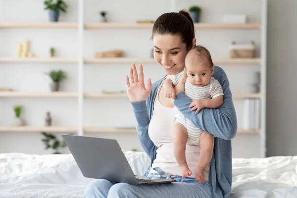 Jeune mère tenant bébé et faisant appel vidéo avec ordinateur portable à la maison — Photo