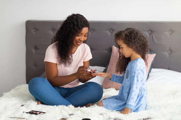 Afroamerikanische Mutter lackiert ihre kleinen Töchter auf dem Bett im Haus, in voller Länge. Zeitvertreib für Familien — Stockfoto