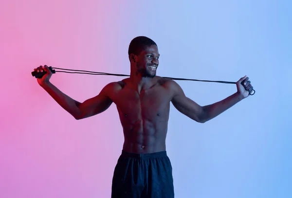 Sorrindo cara preto com corpo muscular segurando pulando corda em luz de néon. Conceito de estilo de vida saudável — Fotografia de Stock