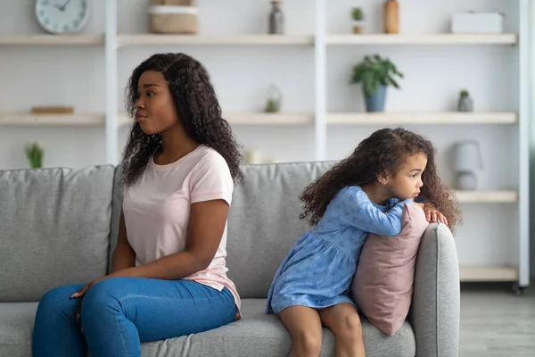 Чорношкіра жінка і її дочка сидять на спині на дивані, не розмовляючи один з одним після бою вдома — стокове фото