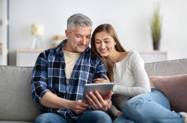 Olgun evli bir çift evdeki koltukta oturup tablet bilgisayar kullanıyor, film izliyor, uzaktan çalışıyor.