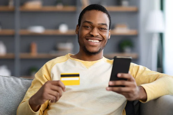 Vrolijke Afrikaans-Amerikaanse man met creditcard en mobiele telefoon — Stockfoto