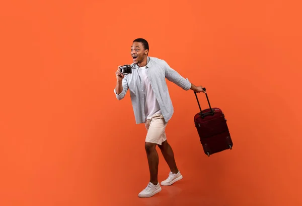 Pełna długość portret podekscytowany czarny facet z syutcase i aparat spaceru na lotnisko, gotowy do rozpoczęcia wakacji — Zdjęcie stockowe