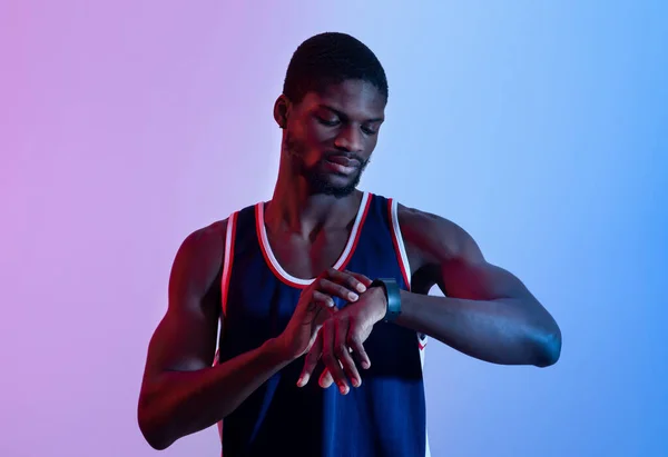 Homem negro atlético em sportswear olhando para seu smartwatch em luz de néon. Tecnologias inovadoras e estilo de vida ativo — Fotografia de Stock