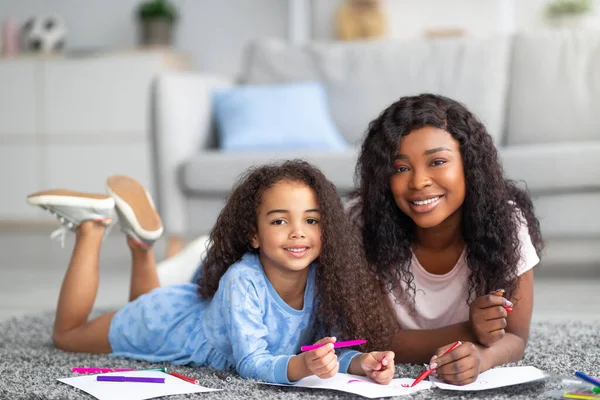 Pozytywna czarna mama i jej szczęśliwa córka rysują razem na podłodze w domu. Koncepcja dziecięcych rozrywek rodzicielskich — Zdjęcie stockowe