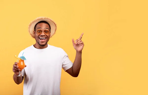 Uma oferta incrível. Homem afro-americano animado com delicioso coquetel de verão apontando para o espaço em branco no fundo amarelo — Fotografia de Stock