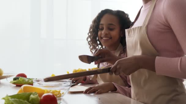 Linda niña afroamericana viendo a su madre preparando ensalada de verduras en la cocina, disfrutando del proceso de cocción — Vídeo de stock