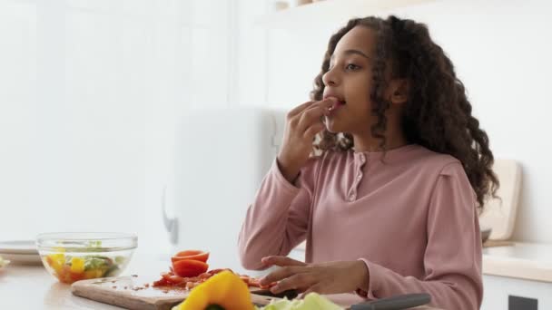 Aranyos kis afro-amerikai lány élvezi a friss bio paradicsom, vágás zöldségek saláta a konyhában — Stock videók