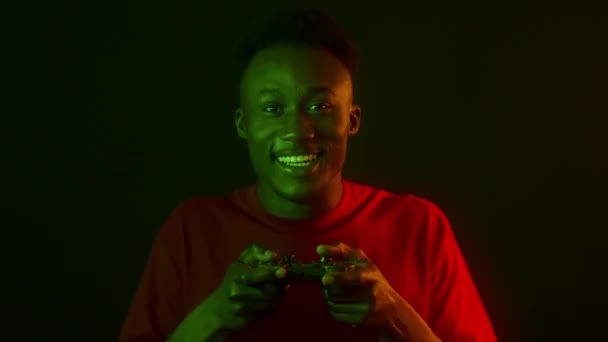 Cyberruimte. opgewonden Afrikaans amerikaanse man spelen video games met joystick, lachen om camera in groene neon lichten — Stockvideo