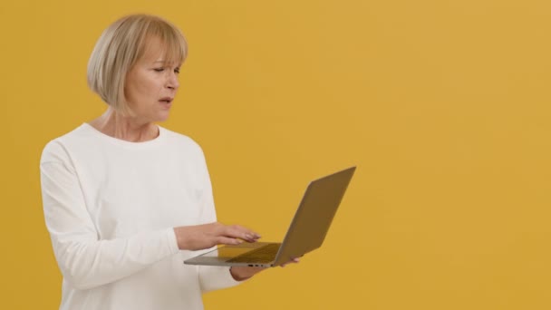 使用笔记本电脑的老太太很不高兴，上网有问题，工作室背景是橙色的，空间空旷 — 图库视频影像