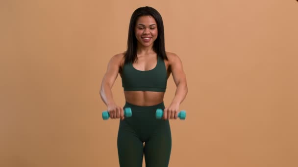 Ejercicio femenino africano levantando pesas durante el entrenamiento sobre fondo beige — Vídeos de Stock