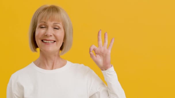 Glada äldre dam ler mot kameran och visar OK gest, känna sig glad, orange bakgrund med tomt utrymme — Stockvideo