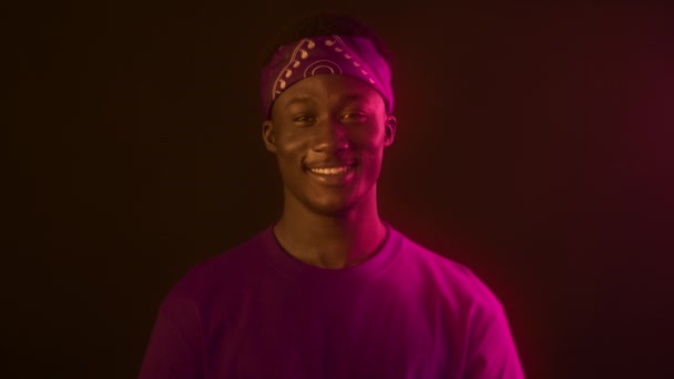 Sign of love. Portrait of happy african american guy showing heart gesture and smiling widely to camera in neon lights — Stock Video