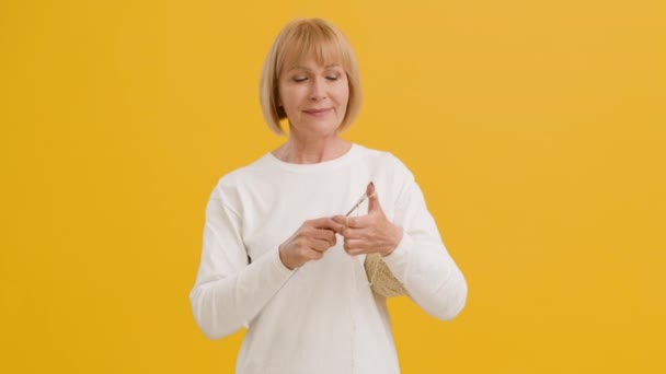 Glücklich positive reife Dame Strickkleidung mit Nadeln und Fadenknäuel, lächelnd in die Kamera, orangefarbener Studiohintergrund — Stockvideo