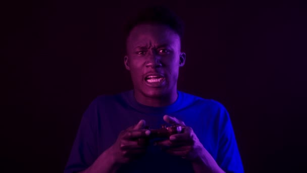 I videogiochi falliscono. Giovane infastidito uomo africano americano con joystick perdere gioco dicendo Vieni in luci viola al neon — Video Stock