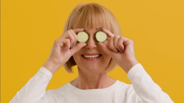 Házi szépségápolás. Pozitív idős hölgy kezében uborka szeletek közel szemek, hogy őket el, és mosolyogva a kamera — Stock videók