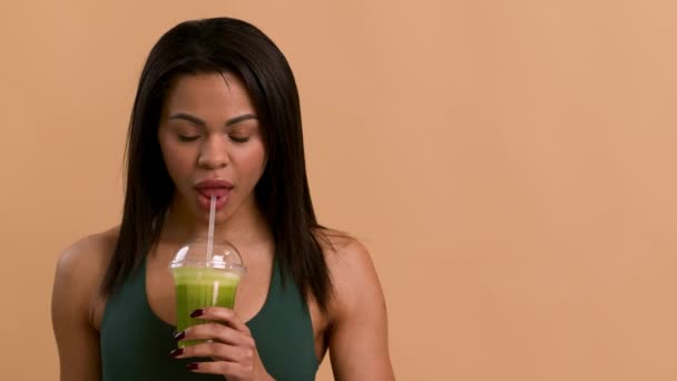 Africana bebiendo batido sonriendo a cámara sobre fondo beige — Vídeos de Stock