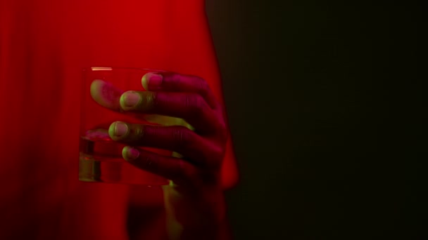 Nightclub atmosphere. Close up of unrecognizable african american guy holding glass with drink, in red neon lights — Stock Video