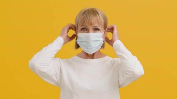 リスクグループに対する予防措置。カメラを真剣に見て、保護医療用マスクを身に着けているシニア女性 — ストック動画