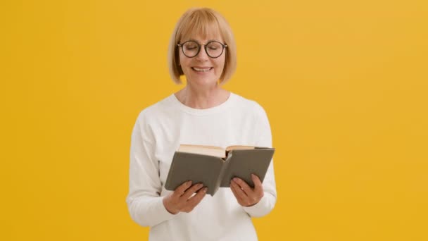 Selbsterziehung. Glückliche Seniorin mit Brille liest Buch und lacht, genießt Lieblingsliteratur, orangefarbener Hintergrund — Stockvideo