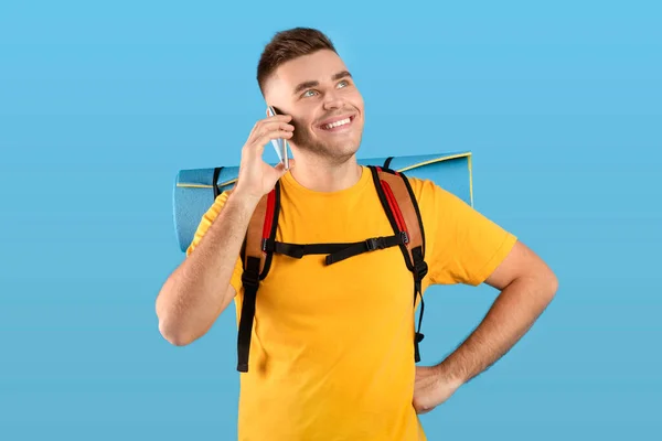 Vonzó Y-generációs srác turista fogaskerekek beszél okostelefonon keresztül kék stúdió háttér — Stock Fotó