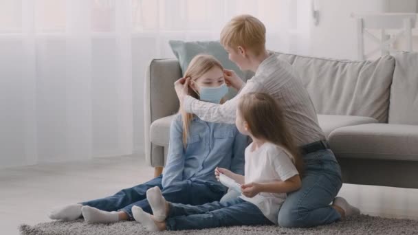 माँ घर पर बेटियों पर सुरक्षात्मक चेहरे मास्क डाल रही — स्टॉक वीडियो