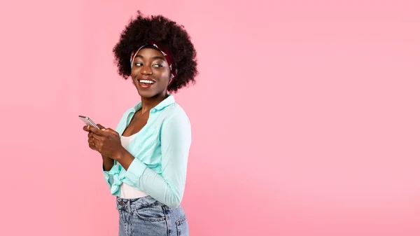 ผู้หญิงแอฟริกันที่มีความสุข ใช้สมาร์ทโฟน ยืนอยู่เหนือพื้นหลังสีชมพู พาโนรามา — ภาพถ่ายสต็อก