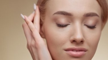 Kadın güzelliği. Güzel sarışın bayan yüzüne dokunuyor ve kameraya gülümsüyor, bej rengi stüdyo arka planı, boş alan.