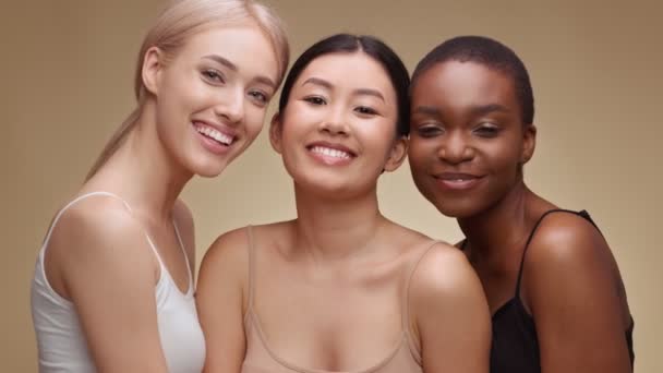 Studio portret van drie gelukkig multi-etnische dames lachen om camera, genieten van vriendschap, knuffelen over beige achtergrond — Stockvideo