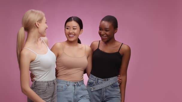Geweldige winkelpromo. Drie verschillende vrouwen kijken opzij en lachen om lege ruimte, glimlachen om camera, roze achtergrond — Stockvideo
