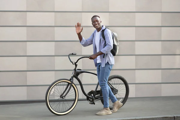 Cara millennial positivo com bicicleta moderna acenando perto da parede de tijolo ao ar livre — Fotografia de Stock