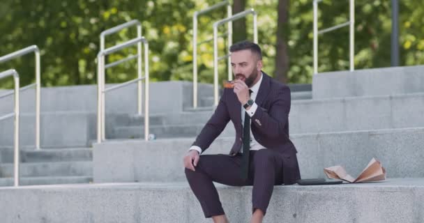 Lente lunchpauze. Gelukkig volwassen zakenman eten pizza, ontspannen op trappen in stedelijk park — Stockvideo