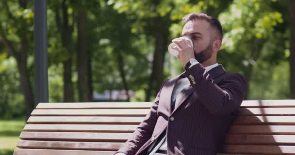 Relaxado homem de negócios maduro sentado no banco no parque, desfrutando de café takeaway quente, atender telefonema e falando — Vídeo de Stock