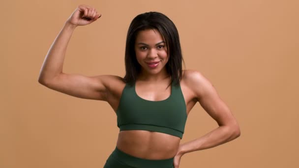 Atlética mujer africana mostrando bíceps músculos posando sobre fondo beige — Vídeos de Stock
