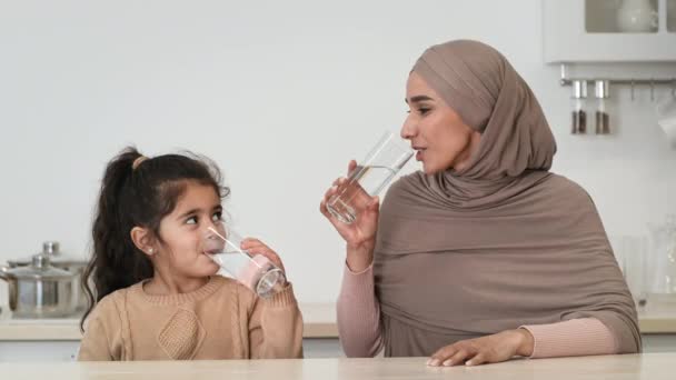 Maman musulmane et petite fille boire de l'eau assis dans la cuisine — Video