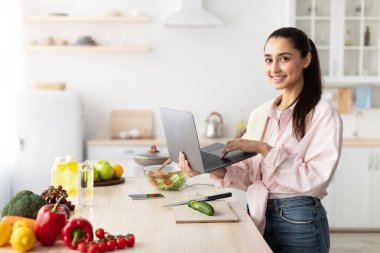 Kadın salata pişiriyor, dizüstü bilgisayar ve mutfak kullanıyor.
