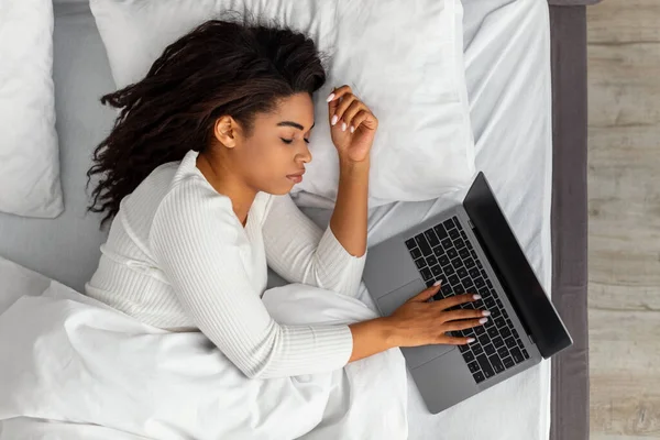 Mujer afroamericana acostada en la cama, durmiendo y sosteniendo la computadora portátil — Foto de Stock