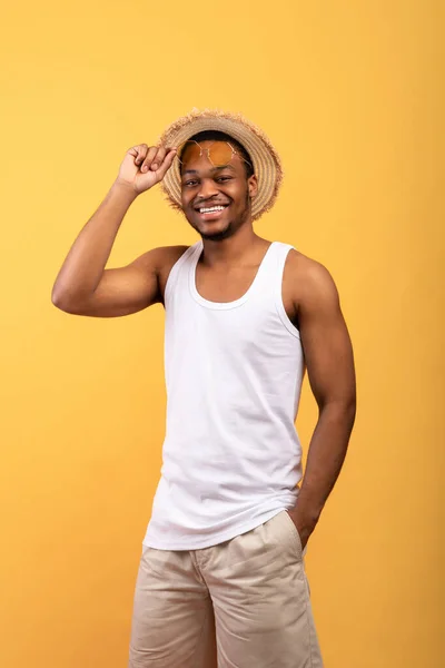 Yaz titreşimleri. Tişörtlü, şortlu, hasır şapkalı, güneş gözlüklü, poz veren ve kameraya gülümseyen genç siyahi adamın portresi. — Stok fotoğraf