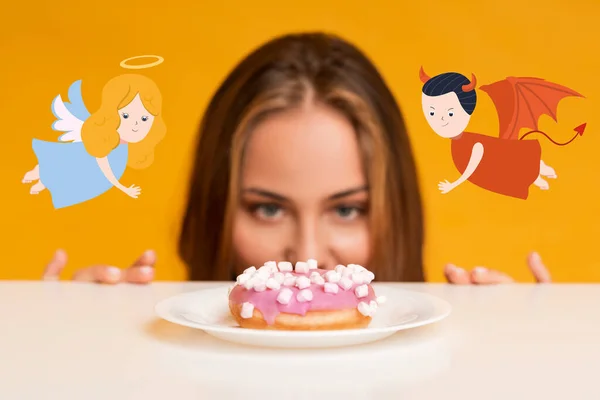 A fiatal nő éhesen nézi a fánkot, meg akarja törni a diétáját, kétkedve az angyal és az ördög javaslatától. — Stock Fotó