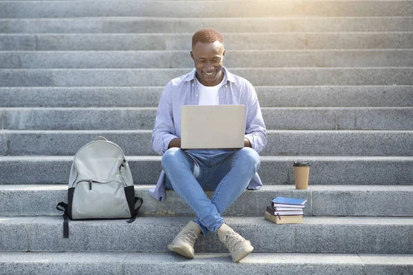 Çalışkan siyahi adam şehir merkezindeki merdivenlerde dizüstü bilgisayarla online çalışıyor.