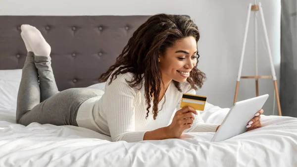 Happy black woman holding debit credit card, using tablet