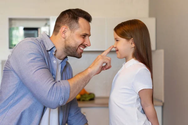 Alegre pai tocando pouco filhas nariz posando na cozinha, vista lateral — Fotografia de Stock