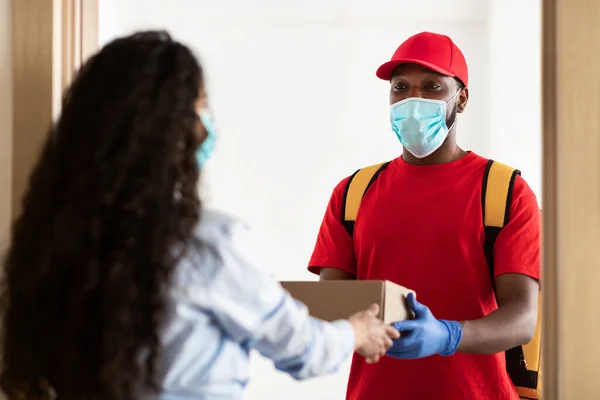 Black delivery man in medical mask giving box to woman — Stock Photo, Image