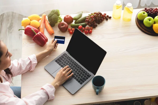 Frau benutzt Laptop mit in der Küche und hält Kreditkarte — Stockfoto