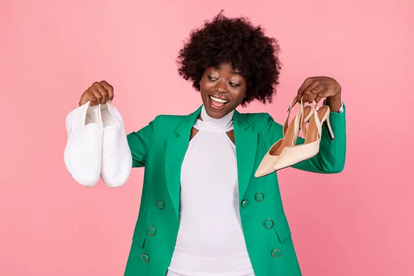 African Lady Holding Sneakers And High-Heels Choosing Shoes, Pink Background