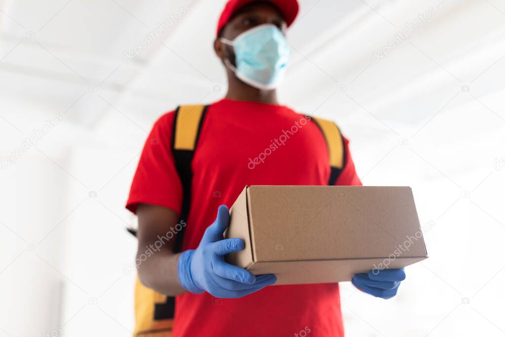 Black delivery man in medical mask giving box