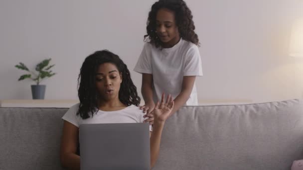 Little african american girl asking her mother for attention, but busy woman working on laptop, sitting on couch at home — Stock Video