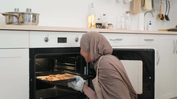 Donna musulmana che cuoce biscotti in piedi vicino al forno nella cucina moderna — Video Stock