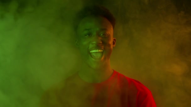 Sucesso e emoção. Cara afro-americano feliz torcendo em fumaça verde e luzes de néon, mostrando gesto de vitória — Vídeo de Stock